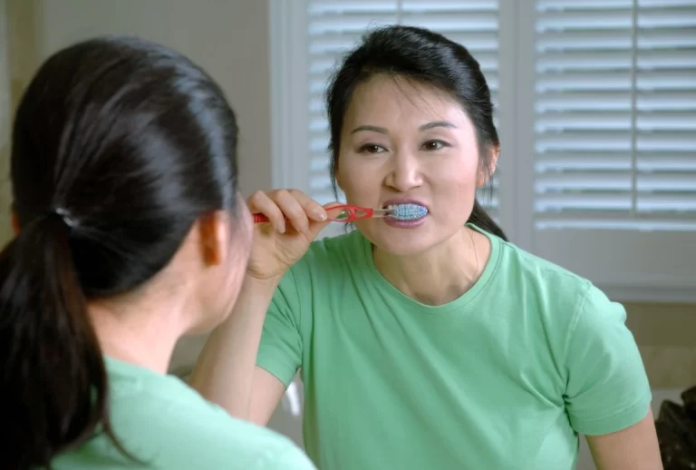 asian lady standing in front of mirror and brushing teeth - Oral Hygiene Tips for Braces: Keeping Your Smile Healthy